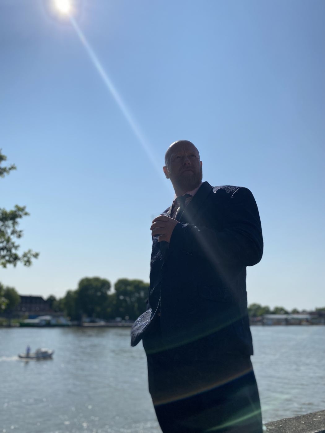Olav Pirmajer im Anzug am Flussufer, im Gegenlicht